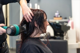 Profile photo of an anonymous hairdresser using hair dryer to dry the hair of a client
