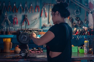 Skilled craftswoman repairing a motorcycle engine part in a workshop with a teal wall, a complete