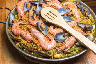 A paella full of seafood, peas, and rice served in a pan with a wooden spoon, typical Spanish