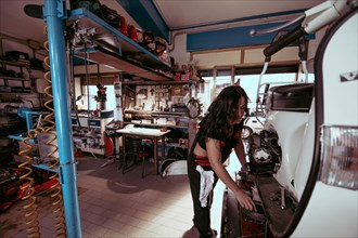 View of a hispanic young long haired brunette female mechanic working diligently in a packed
