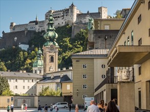 View of a historic castle above the city with a clear sky and people in the foreground Salzburg