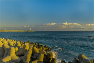 A lighthouse oversees the calm sea with tetrapods used for coastal protection at dusk, in South