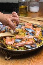 Hand gently stirring a seafood paella with shrimp and mussels using a wooden spatula, typical