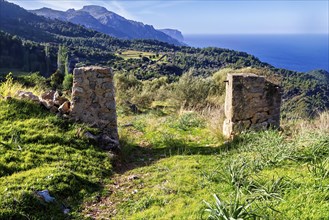 Stone pillars frame a rural scene with green fields and distant mountains, Hiking tour from