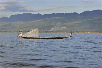 Fisherman in traditional boat working on a lake, mountains in the background, Inle Lake, Myanmar,