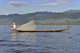 Fishermen on a boat in sunny weather, picturesque mountain scenery in the background, Inle Lake,