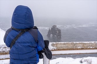 Adventurous woman in winter in Iceland looking at the frozen figure of Hvitserkur