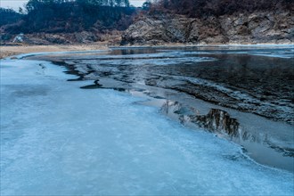 Close-up of cracked ice on a frozen river with forest in the background, in South Korea