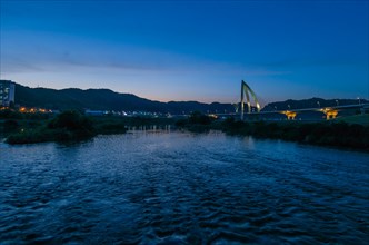 Twilight at a riverfront with bridge and cityscape reflections in blue tones, in South Korea