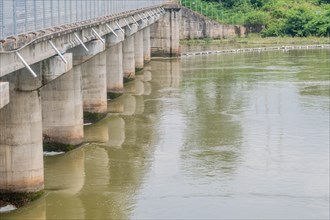 A sturdy concrete bridge spans across a wide river, reflected on the water's surface, in South