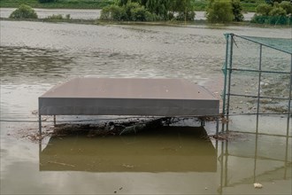 Top of benches submerged by flood water at baseball diamond in riverside park after torrential