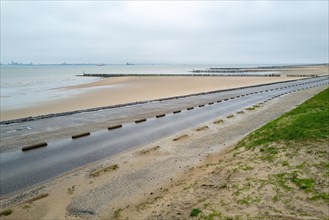 View of beach defence structures along a wet coastal road under cloudy skies, Breskens, Zeeland,