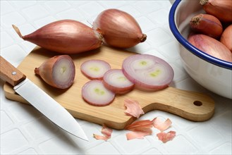 Sliced shallots on a wooden board with a knife, Allium cepa