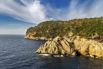 Rugged cliffs with greenery overlooking calm blue ocean under a partly cloudy sky, Peguera,