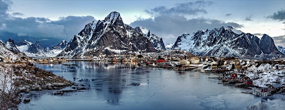 Twilight over a snowy fishing village with mountains reflected on the water, Lofoten