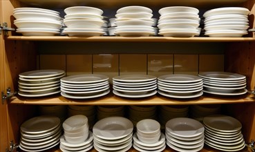 Neatly stacked plates and dishes in a wooden kitchen cabinet with open doors AI generated