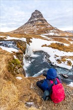 Adventurous photographer woman in winter in Iceland photographing sitting at the Kirkjufell