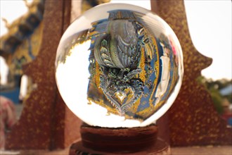 Glass ball reflecting the inverted image of Wat Rong Suea Ten or Blue Temple in Chiang rai Thailand