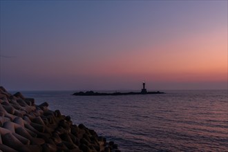 Evening view of a lighthouse seen over a breakwater under a purple dusk sky, in South Korea