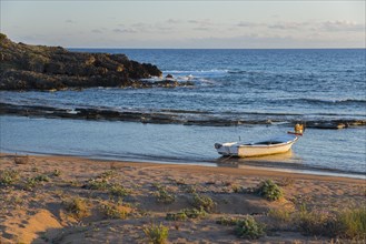 Tranquil scene of a single boat on the coastline with rocks in the soft evening light, Finikounda,