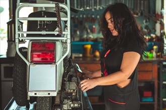 A hispanic young sensual female mechanic inspecting a rear car light in an automotive workshop,