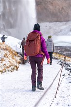 A woman visiting Iceland in winter with a backpack at the Seljalandsfoss waterfall