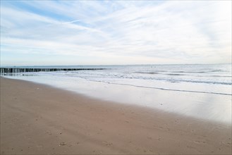 Empty beach overlooking a calm sea, damp sand reflects the sky