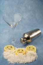 Lemon slices with cloves and cinnamon forming a smiley face on a pile of salt next to a cocktail