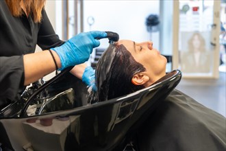 Hairdresser washing the hair of a client lying on sink in a hair salon