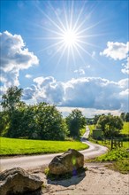 A rural scene with a path, rocks and bright sun in a partly cloudy sky, Wuelfrath, Mettmann,