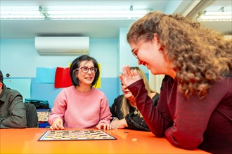 Caregiver and woman with special needs playing with board games on a table of a day center