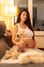 Vertical portrait of a dog lying on lap of pregnant woman on the sofa at night