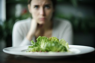 Plate with salad and frustrated hungry woman on diet in blurry background. KI generiert, generiert