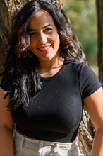 Joyful Cheerful hispanic young woman with a beaming smile in a black shirt outdoors, blurred
