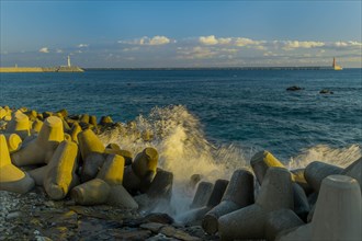 Shoreline with tetrapods as waves break under a clear blue sky with a lighthouse, in South Korea