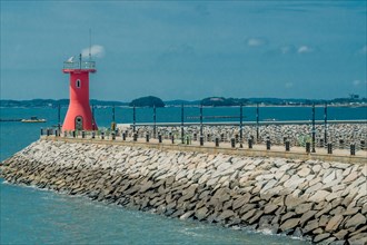 Red lighthouse on end of concrete pier in seaside fishing port in South Korea