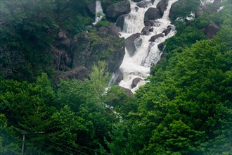 Misty waterfall flowing through a rocky landscape with surrounding greenery, in South Korea