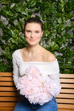 Smiling woman sits on a wooden bench with a bouquet of spring pink flowers