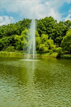 Vertical jet of water from a fountain in a serene pond surrounded by park greenery, in South Korea