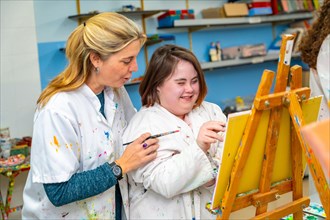 Adult caucasian teacher helping a smiling woman with down syndrome during painting class