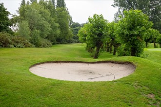 Sand bunker on a green golf course with trees and a cloudy sky