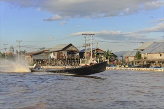 Fishing boat passes stilt houses of a waterfront village, Pindaya, Inle Lake, Myanmar, Asia