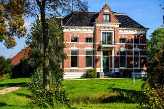 A traditional country house surrounded by trees under a blue sky with clouds, Winschoten,