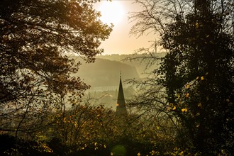 Mystical view of a church tower through foggy, autumnal trees in the backlight, Arrenberg,