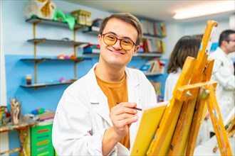 Portrait of a happy man with down syndrome smiling at camera during painting class