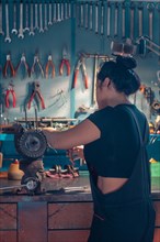 Woman mechanic repairing an alternator at a workbench in an auto moto workshop, wearing black