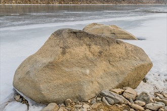 A large rock on the snowy bank of a partially frozen river, in South Korea