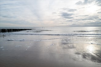 View of the calm sea with foam waves, breakwaters and cloudy sky