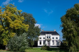 Elegant white villa against a clear blue sky, surrounded by lush gardens, Winschoten, Groningen,