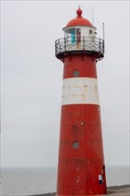 Red and white lighthouse stands against an overcast sky on the seashore